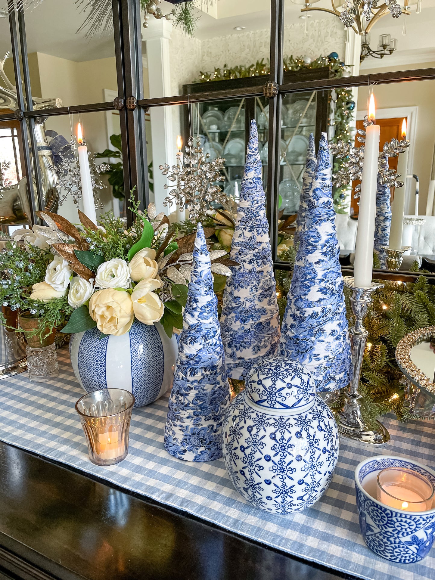 Decorative table setting with blue and white ceramic trees, candles, and flowers in a home interior.