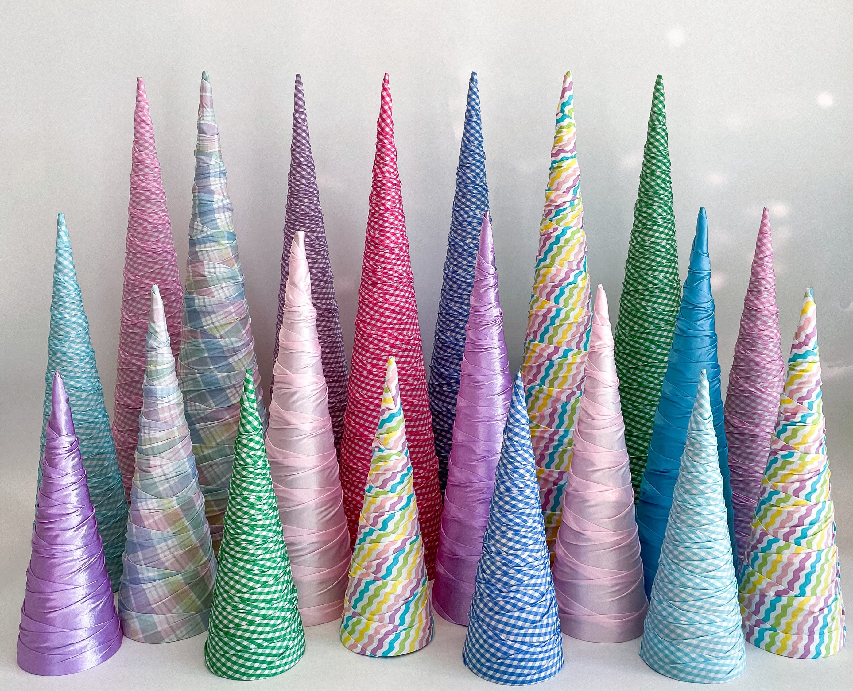 A collection of fabric-wrapped paper mache cones designed to resemble trees, displayed in a variety of pastel colors.